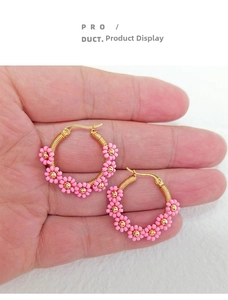 Détail de créoles artisanales en fil d'or avec fleurs en perles roses tenues à la main