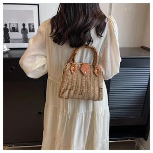 Detail of woven straw handbag featuring a bamboo U-shaped handle and leather fasteners