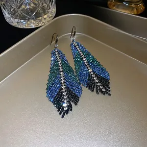 Exaggerated rhinestone feather drop earrings in blue and green gradient on a tray
