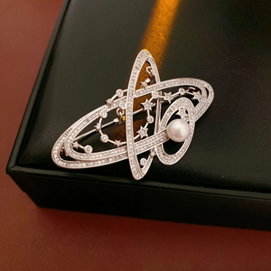 Macro shot of silver planet brooch with white pearl and sparkling zircons on black leather