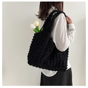 Detail of black popcorn texture tote bag worn on shoulder by model with white tulips