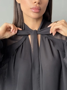 Close-up of black chiffon blouse featuring an elegant bow tie neckline and sheer fabric