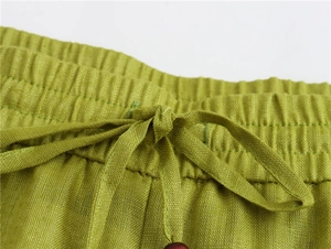 Dettaglio dei pantaloni in lino verdi con vita elastica, coulisse e una perla di legno