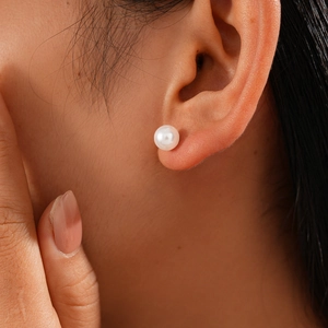 Close-up of a white round pearl stud earring worn on model's ear showing realistic fit