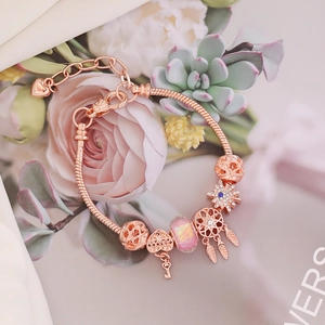 Rose gold owl charm bracelet with heart, feather, and pink beads on a romantic background