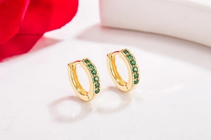Macro shot of gold hoop earrings set with green stones next to red flower petals