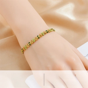 Detail of a 18K gold-plated leaf chain bracelet with green enamel on champagne silk