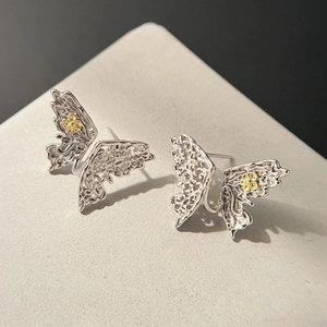 Detailed close-up of hollow silver butterfly stud earrings with gold flower accents