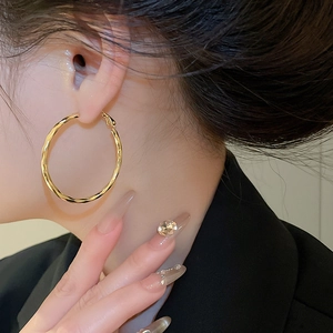 Detailed close-up of 14k gold plated twisted hoop earrings worn on a model with a black suit