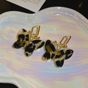 Detailed macro view of golden butterfly earrings with leopard print wings on a tray