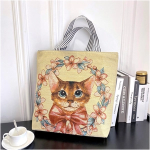 Detail of beige canvas tote bag with cat floral print and striped handles in lifestyle setting