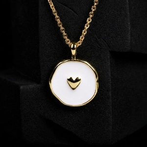 Detail shot of a gold heart pendant with white enamel inlay on a black textured cube