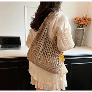 Detail of beige hollow knit tote bag with yellow tassel on a model's shoulder