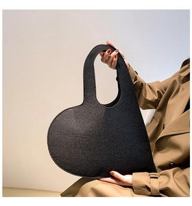 Detail shot of heart-shaped black felt handbag held by a model in a trench coat