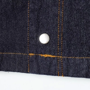 Detailaufnahme von dunkelblauem Denim mit orangen Nähten und silberner Metallniete