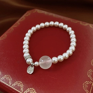 Close-up of white crystal bead bracelet with pink centerpiece and silver charm on red box