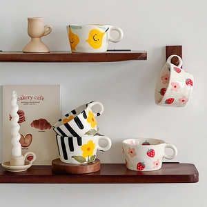 Detail showing hand-pinched ceramic mugs with colorful hand-painted fruit and floral motifs