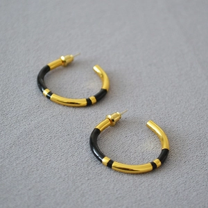 Macro shot of minimalist gold-plated C-shaped earrings with black enamel detail