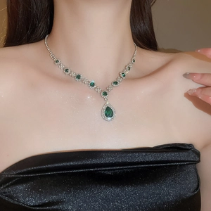 Close-up of a silver-toned necklace with a large pear-cut green gemstone and diamonds