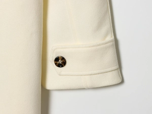 Detail of cream white wool coat cuff featuring a decorative amber tortoiseshell button