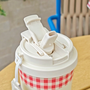 Close-up of portable red checkered coffee cup with flip straw lid and white woven lanyard