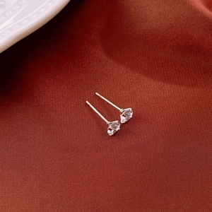 Macro shot of silver zircon stud earring with four-claw setting on textured fabric