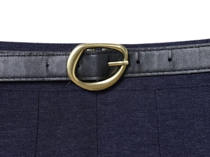 Dettaglio della fibbia dorata su cintura in pelle nera e gonna a pieghe blu scuro