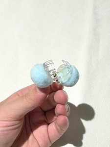 Detail of light blue fluffy pompom hair clip with transparent claw and metal spring