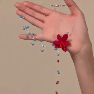 Detail einer blauen Perlenkette mit einer roten 3D-Blume, in der Hand gehalten