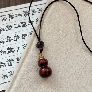 Detail showing the polished dark reddish-brown wooden double gourd pendant with a mystic knot