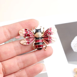 Detail of a handmade bee brooch featuring colorful gradient enamel wings and gold base