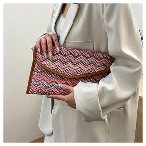 Detail of bohemian envelope straw clutch with colorful wave patterns and brown leather trim