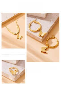 Detail view of matte gold butterfly necklace, earrings, and open ring set on a stone surface