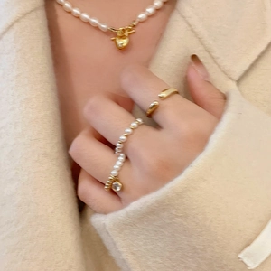 Ensemble de bagues dorées et collier de perles avec pendentif cœur sur maille beige