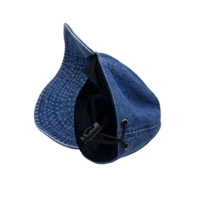 Detail view of adjustable black drawstring and metal eyelet on washed blue denim cap
