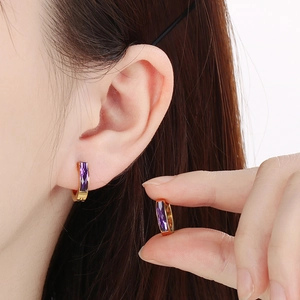 Detail of gold hoop earrings with rectangular purple zircon worn by a model