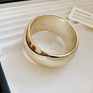 Vue détaillée d'un large bracelet doré évidé placé sur un plateau à bijoux blanc texturé