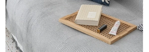 Rectangle wooden serving tray with rattan mesh bottom on grey waffle weave blanket