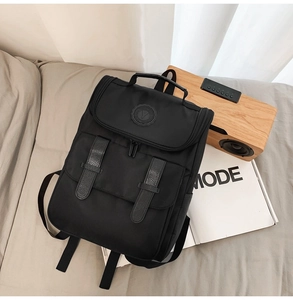 Flat lay of a black nylon backpack with decorative leather straps on a modern bed