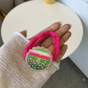 Close-up of pink fabric hair tie with a round landscape oil painting charm detail