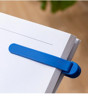 Detail of blue silicone auto-tracking bookmark clipped to white paper for easy reading