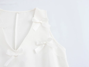 Détail d'une robe blanche sans manches à col en V avec nœuds délicats et tissu texturé