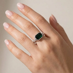 Detail view of a vintage silver ring featuring a rectangular emerald green gemstone and twisted band