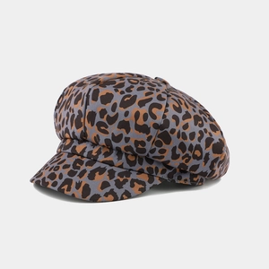Detailed view of leopard print baker boy cap with brown and black patterns on grey fabric