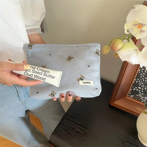 Macro detail of a light blue corduroy makeup bag with cute bear embroidery and brand label