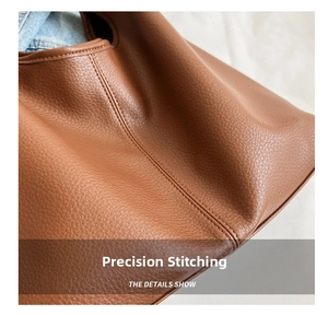 Detail view of double stitching and lychee grain texture on a brown leather tote bag