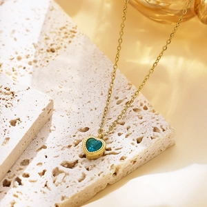 Macro shot of blue heart zircon pendant on golden chain resting on beige travertine stone