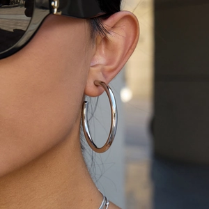 Polished silver stainless steel C-hoop earring worn by a model in outdoor setting