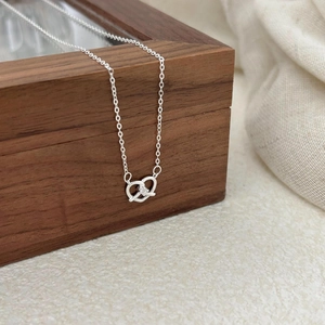 925 silver pretzel pendant necklace with white zircon on a vintage wooden jewelry box