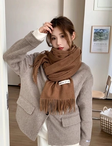 Detailed view of soft brown solid color scarf with tassels worn in a warm indoor setting